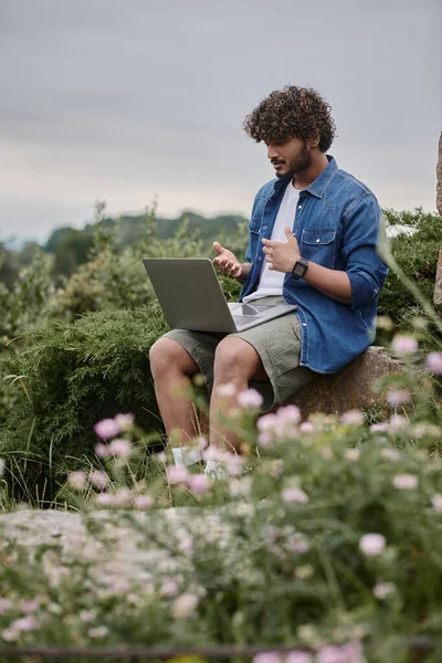 Digital nomad concept, curly indian freelancer having video call on laptop in natural location — Stock Photo