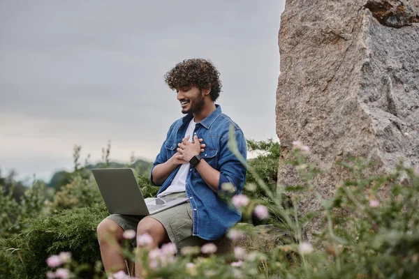 Digital nomad concept, joyful indian freelancer having video call on laptop in natural location — Stock Photo