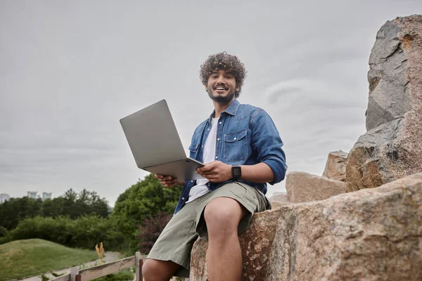 Glücklicher indischer Freiberufler, der aus der Ferne arbeitet und Laptop am natürlichen Ort nutzt, digitaler Nomadentum — Stockfoto