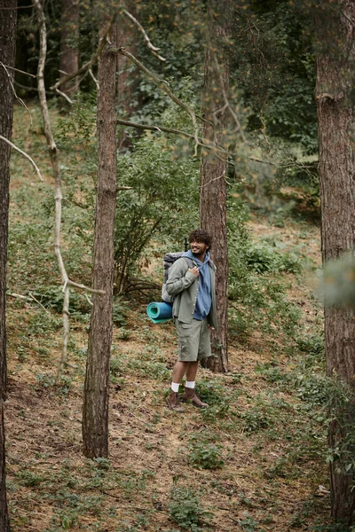 Happy indian backpacker with curly hair walking in forest, natural location, hiker with backpack — Stock Photo
