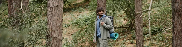 Mochilero indio con pelo rizado caminando en el bosque, ubicación natural, excursionista con mochila, pancarta - foto de stock