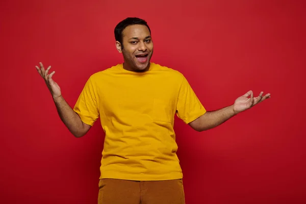 Emotional indian man in bright casual clothes gesturing and talking on red background in studio — Stock Photo