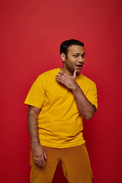 Vertrauter indischer Mann in heller Freizeitkleidung blickt in die Kamera und posiert auf rotem Hintergrund — Stockfoto