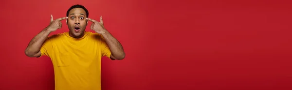 Mind blowing, shocked indian man with fingers near head looking at camera on red backdrop, banner — Stock Photo