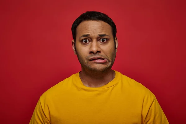 Worried indian man in bright clothes looking at camera and grimacing on red background, stroke — Stock Photo