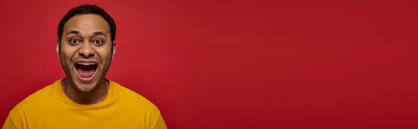Emoção positiva, homem indiano animado em camiseta amarela com boca aberta no fundo vermelho, banner — Fotografia de Stock