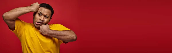 Expression du visage, homme indien en t-shirt jaune se frappant le visage sur fond rouge, bannière — Photo de stock