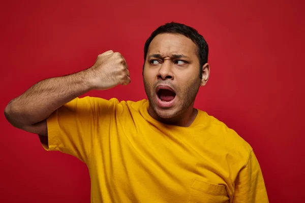 Expresión de la cara, hombre indio emocional en camiseta amarilla golpeándose en la cara en el fondo rojo - foto de stock