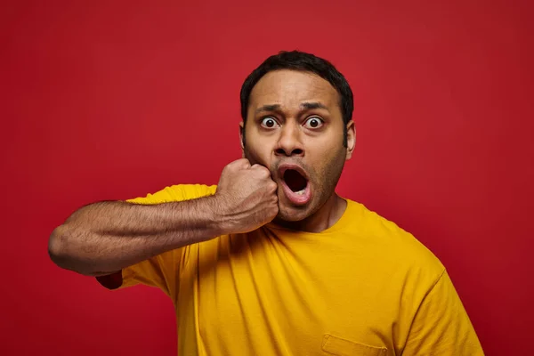 Cara expressão, indiana chocado homem em amarelo t-shirt perfurando-se no rosto no fundo vermelho — Fotografia de Stock