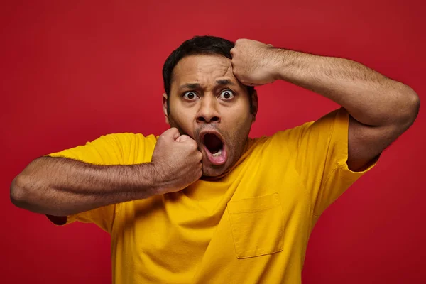 Cara expressão, indiana chocado homem em amarelo t-shirt perfurando-se no rosto no fundo vermelho — Fotografia de Stock