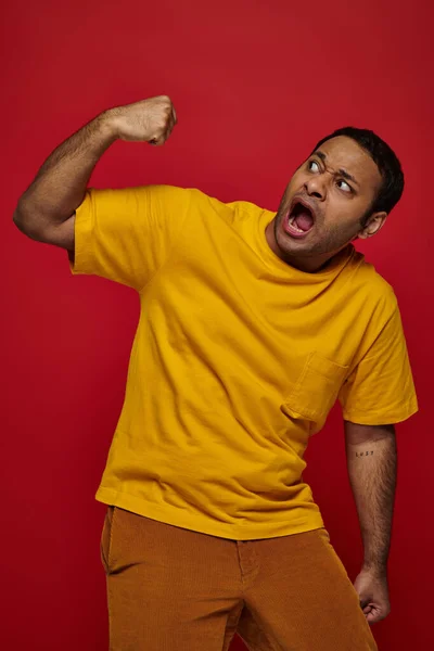 Expresión de la cara, hombre indio asustado en camiseta amarilla golpeándose en la cara en el fondo rojo - foto de stock