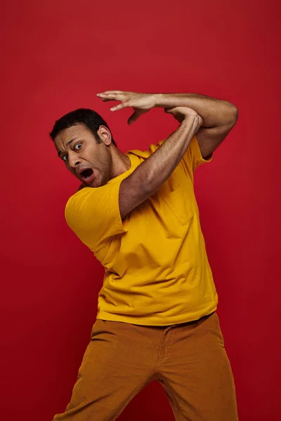 Вираз обличчя, рука наляканого індійця в жовтій футболці, що атакує його на червоному тлі — стокове фото