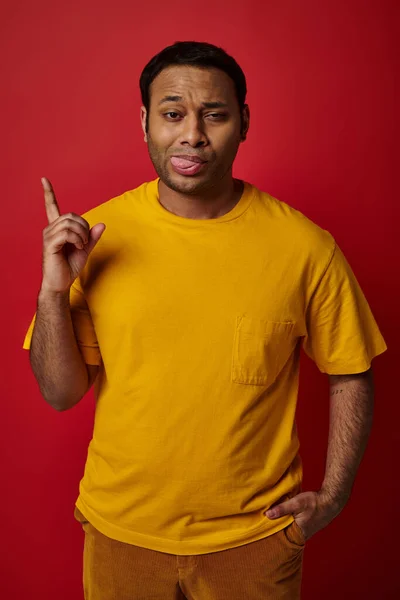 Face expression, emotional man sticking out tongue and pointing up on red background, grimace — Stock Photo