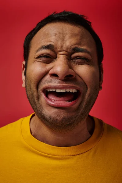 Expressão facial, homem indiano emocional em camiseta amarela chorando alto no fundo vermelho, boca aberta — Fotografia de Stock