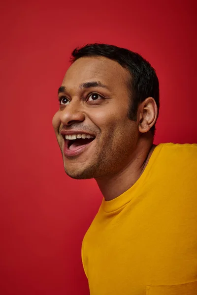 Expresión de la cara, hombre indio sorprendido en camiseta amarilla riendo sobre fondo rojo, boca abierta - foto de stock