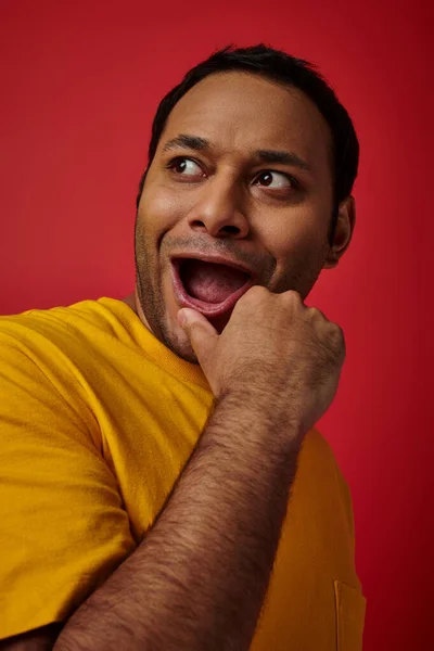 Expression wow, homme indien étonné en t-shirt jaune regardant loin avec bouche ouverte sur fond rouge — Photo de stock
