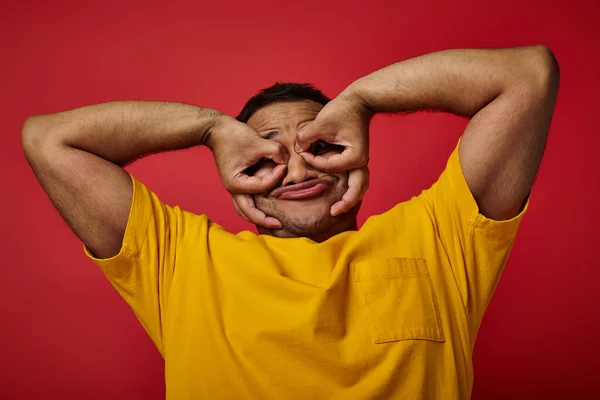 Engraçado indiana homem em amarelo t-shirt risonho e gestos no fundo vermelho, expressivo rosto — Fotografia de Stock