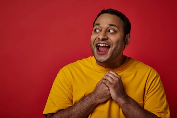 Étonné homme indien avec les yeux grands ouverts regardant loin sur fond rouge en studio, concept surprise — Photo de stock