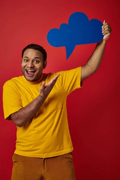 Animado indiana homem em amarelo t-shirt apontando em branco pensamento bolha no fundo vermelho, feliz rosto — Fotografia de Stock