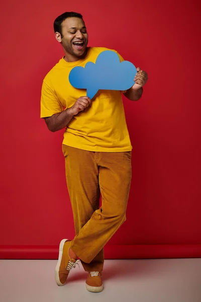Happy man in yellow t-shirt holding blank thought bubble on red backdrop, cheerful face — Stock Photo