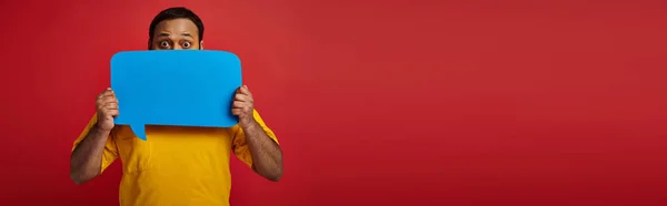 Indian man with eyes wide open hiding behind blank speech bubble on red background, emotion, banner — Stock Photo