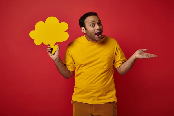 Discouraged indian man holding blank speech bubble and showing shrug gesture on red background — Stock Photo