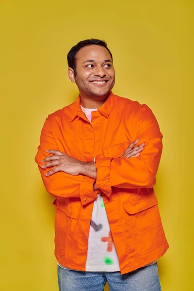 Porträt eines positiven indischen Mannes in orangefarbener Jacke mit verschränkten Armen auf gelbem Hintergrund — Stockfoto