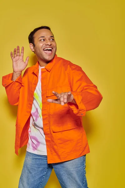 Portrait of astonished indian man in orange jacket and diy t-shirt gesturing on yellow backdrop — Stock Photo