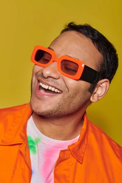 Concepto de auto-expresión, hombre indio feliz en gafas de sol de color naranja brillante sonriendo en el fondo amarillo - foto de stock