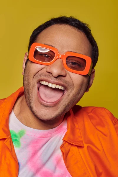 Conceito de auto-expressão, homem indiano animado em óculos de sol laranja sorrindo no fundo amarelo — Fotografia de Stock