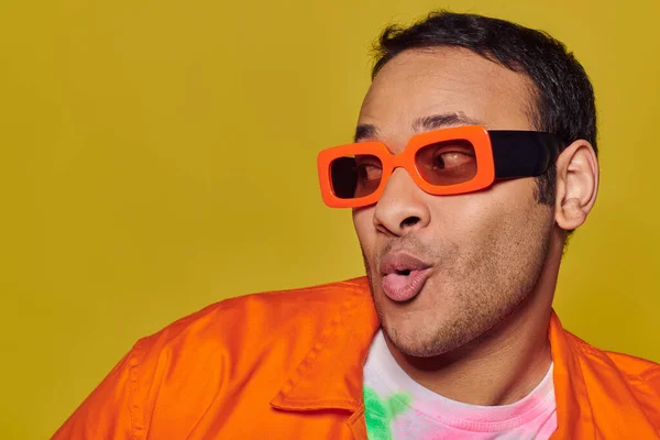 Conceito de auto-expressão, homem indiano surpreso em óculos de sol laranja olhando para o fundo amarelo — Fotografia de Stock