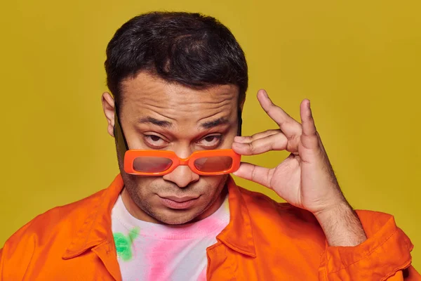 Conceito de auto-expressão, homem indiano confiante ajustando óculos de sol laranja no fundo amarelo — Fotografia de Stock