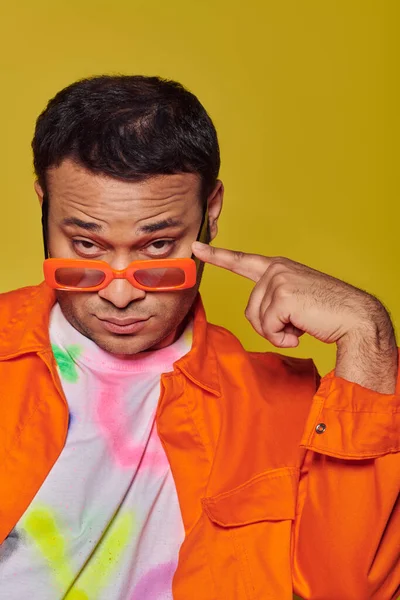 Auto-expressão, homem indiano confiante ajustando óculos de sol laranja no fundo amarelo, ícone de estilo — Fotografia de Stock