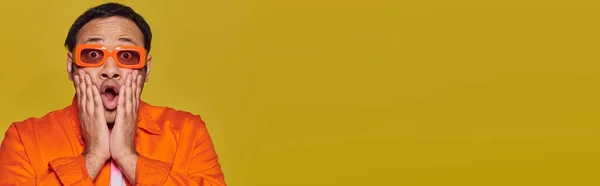 Schockierter indischer Mann mit orangefarbener Sonnenbrille berührt Gesicht und sagt wow auf gelbem Hintergrund, Banner — Stockfoto