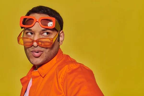 Fashionable indian man trying on different trendy sunglasses and looking away on yellow backdrop — Stock Photo