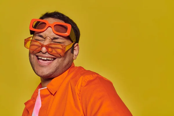 Fashionable indian man trying on different trendy sunglasses and smiling on yellow backdrop — Stock Photo