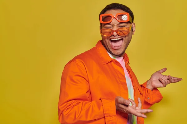 Funny face, excited indian man trying on different trendy sunglasses and smiling on yellow backdrop — Stock Photo
