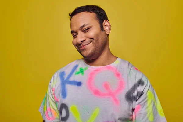 Heureux homme indien en t-shirt vibrant souriant et regardant la caméra sur fond jaune, style personnel — Photo de stock