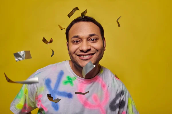 Homem indiano positivo sorrindo perto de cair confete no fundo amarelo, conceito de festa, rosto feliz — Fotografia de Stock
