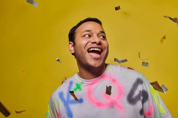 Aufgeregter Indianer lächelt neben fallendem Konfetti auf gelbem Hintergrund, Party-Konzept, glückliches Gesicht — Stockfoto