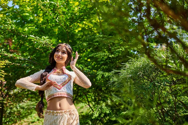 Молодая и счастливая индийская женщина в традиционных танцах во время летних прогулок в парке — стоковое фото