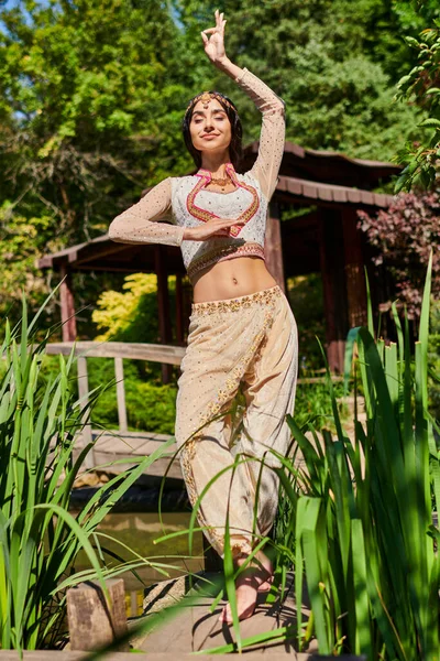 Verano relajarse, elegante mujer india en ropa tradicional bailando con los ojos cerrados en el parque verde - foto de stock