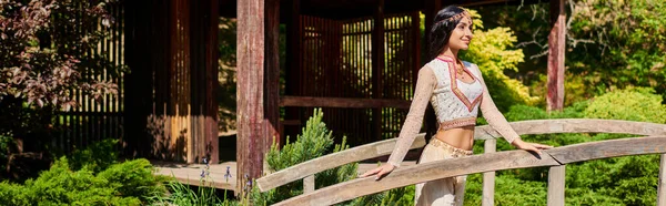 Junge elegante Indianerin in authentischer Kleidung steht auf Holzbrücke im Sommerpark, Banner — Stockfoto