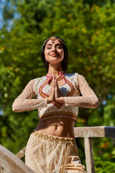 Mujer de estilo auténtico complacido posando con las manos de oración en el parque durante la excursión de verano - foto de stock