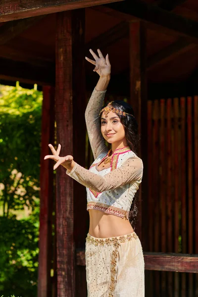 Carefree and elegant indian woman in traditional attire dancing on summer day in park — Stock Photo