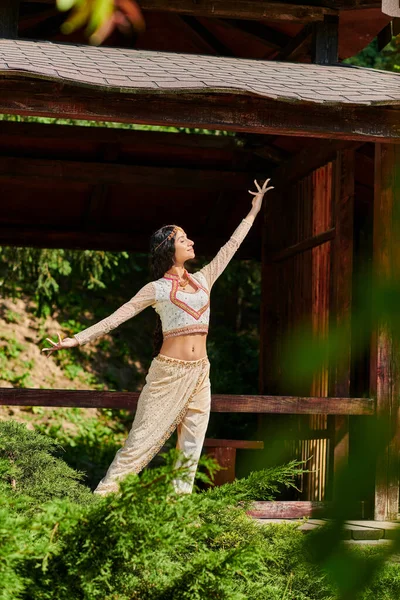 Parco estivo, donna indiana in elegante abbigliamento etnico ballare vicino alcova di legno nel parco estivo — Foto stock