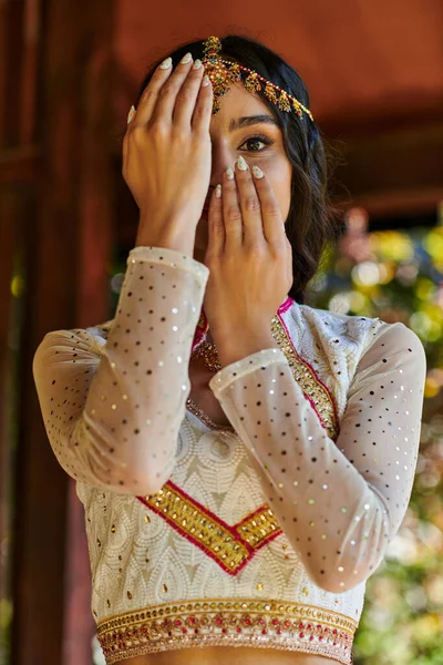 Elegant indian woman in traditional clothes obscuring face with hands and looking at camera — Stock Photo