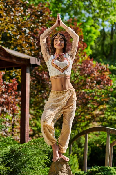 Радостная индийская женщина в элегантной этнической одежде стоя с поднятыми молитвенными руками, летнее счастье — стоковое фото