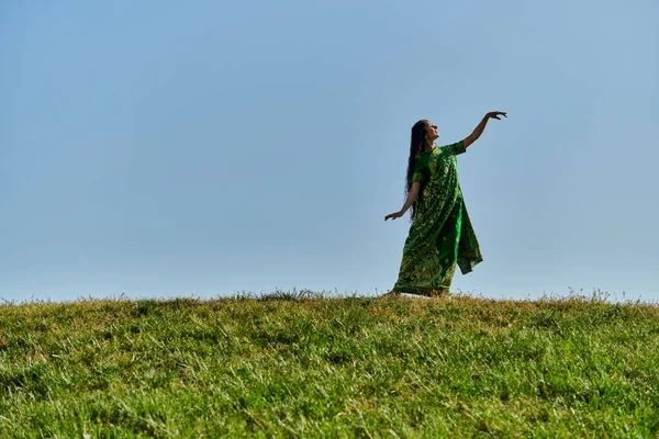 Autenticidade, prazer, mulher indiana feliz em sari no prado verde sob o céu azul, dia de verão — Fotografia de Stock