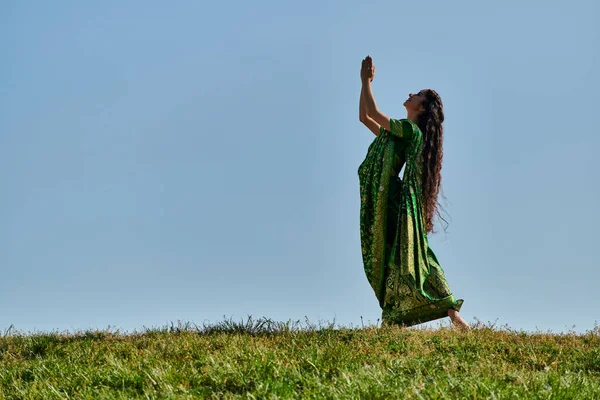 Alegría de verano, mujer india en ropa auténtica, con las manos de oración en el césped verde bajo el cielo azul - foto de stock